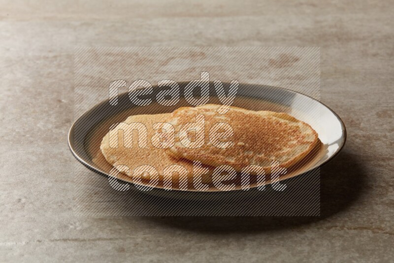 Two stacked plain pancakes in a bicolor plate on beige background