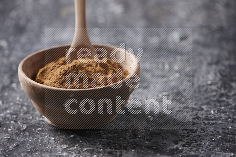 Wooden bowl full of cinnamon powder with a wooden spoon on a textured black background in different angles