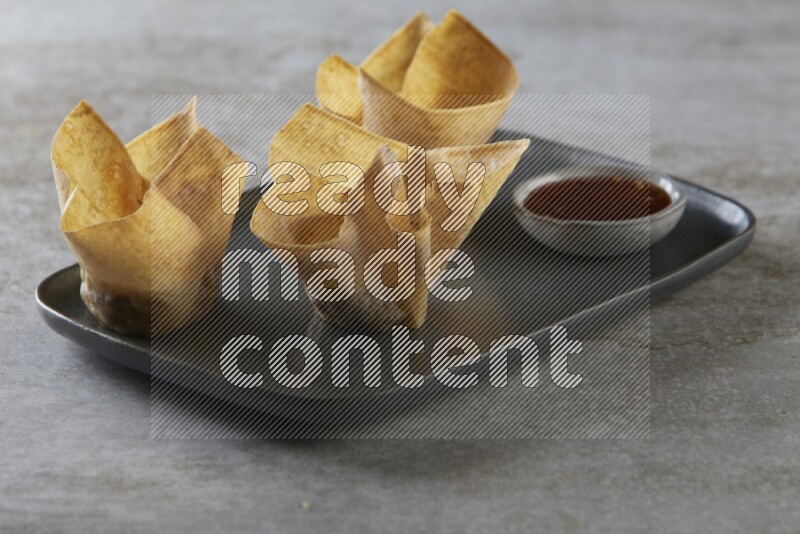 wonton cups with soy sauce ramkin on rectangle dark grey ceramic plate on grey textured counter top