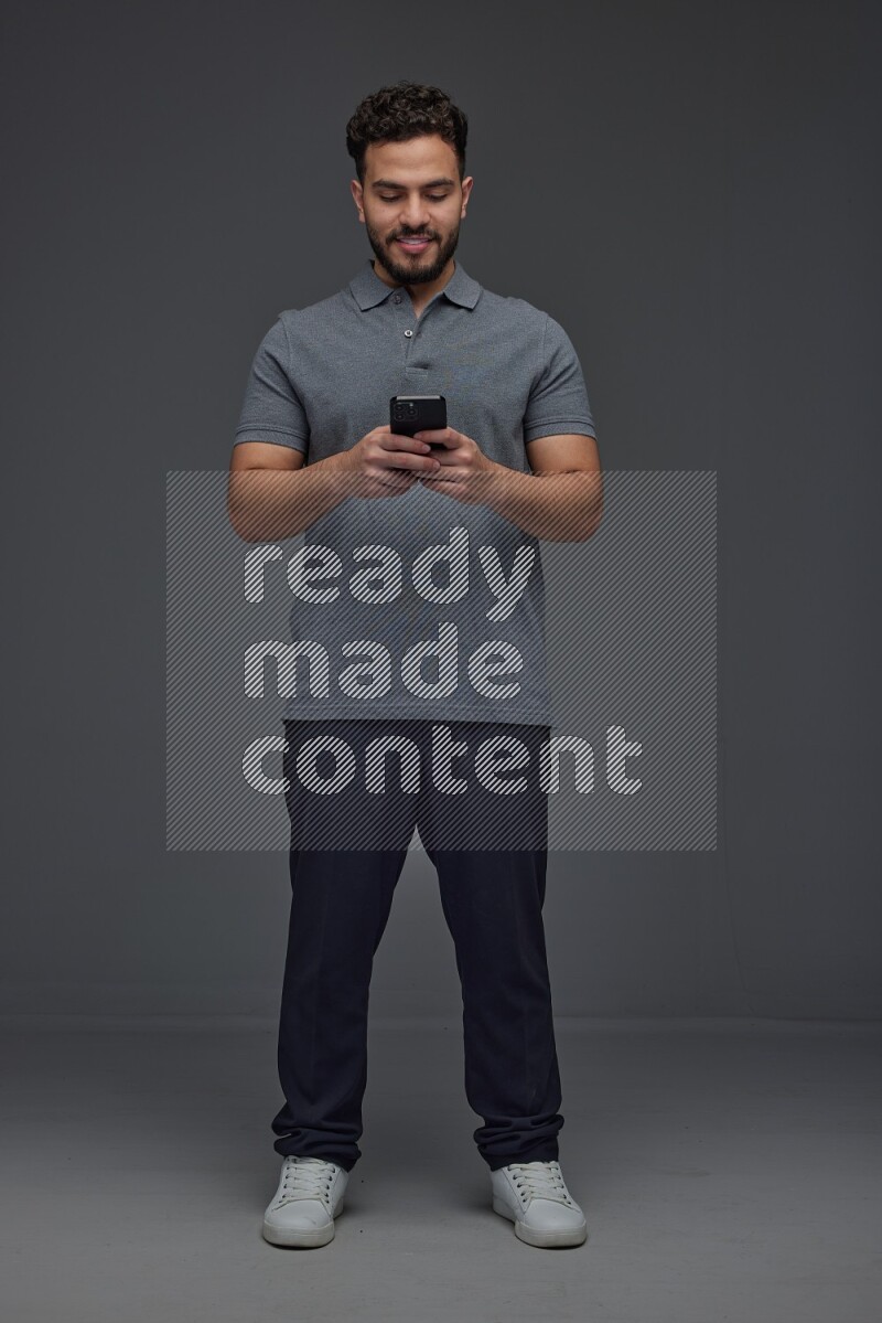 A man wearing casual standing and using his phone eye level on a gray background