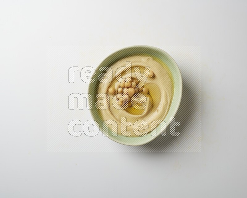 Hummus in a green plate garnished with roasted chickpeas  on a white background