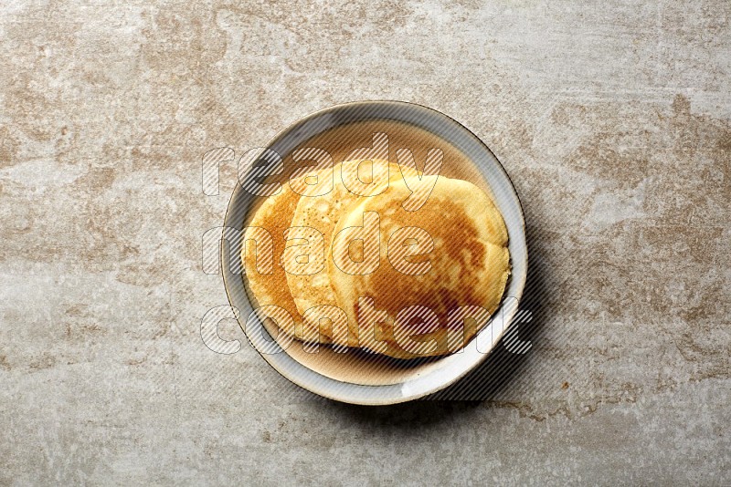 Three stacked plain pancakes in a bicolor plate on beige background
