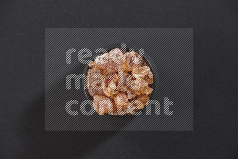 A black pottery bowl full of gum arabic on black flooring