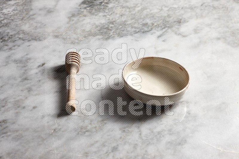 Beige Pottery Bowl with wooden honey handle on the side with grey marble flooring, 45 degree angle