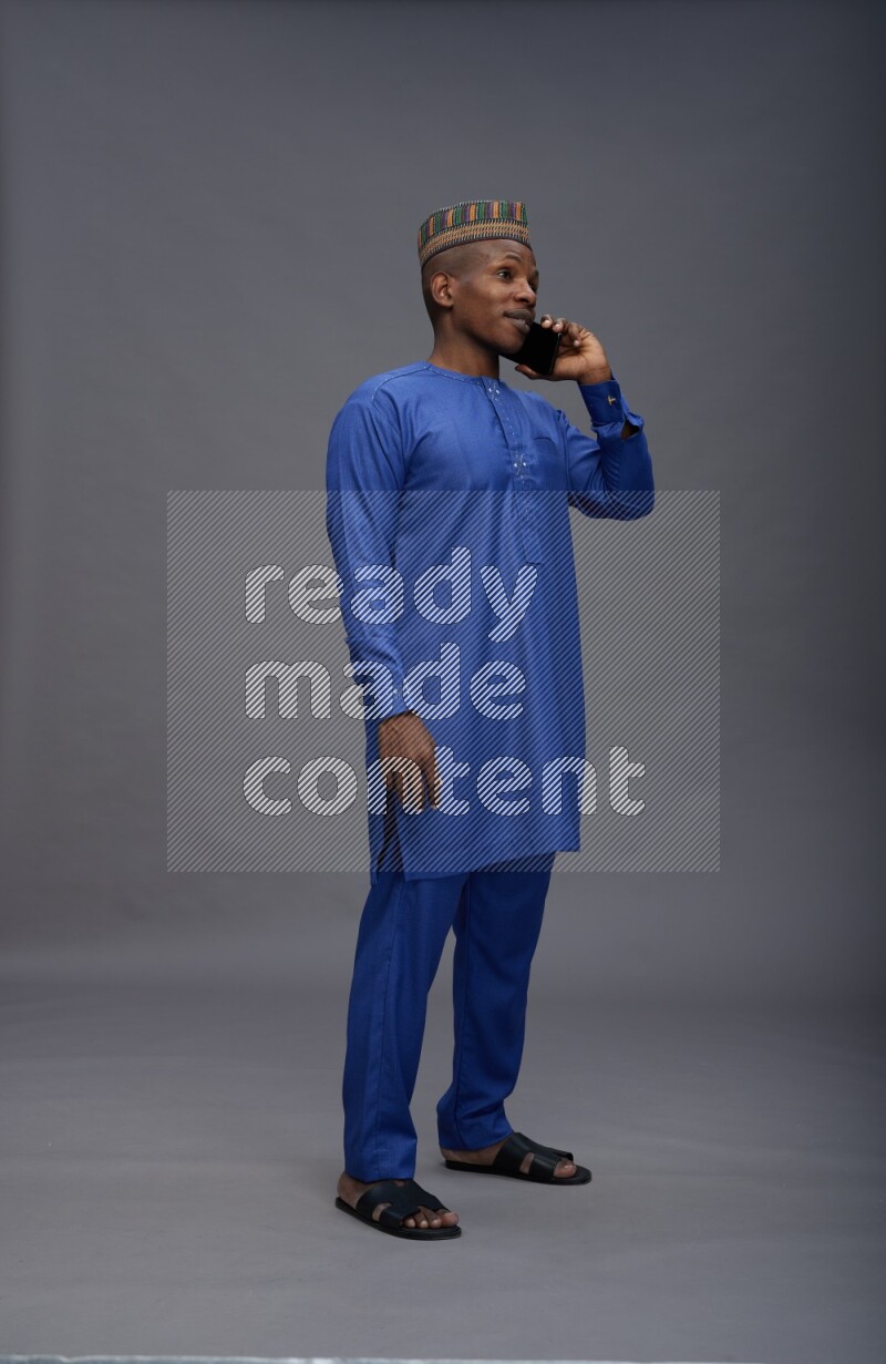 Man wearing Nigerian outfit standing talking on phone on gray background