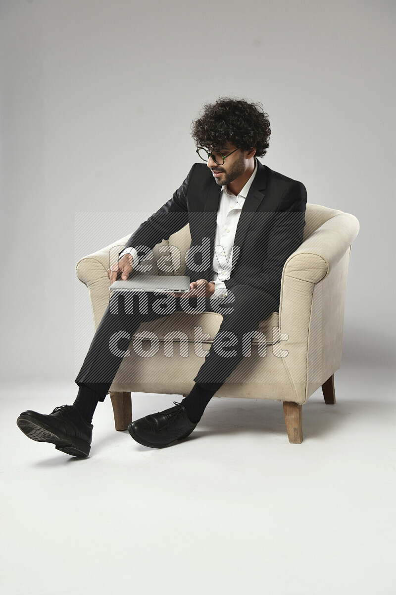 رجل يرتدي ملابس رسمية يجلس علي كرسي و يحمل لاب توب علي خلفية بيضاء