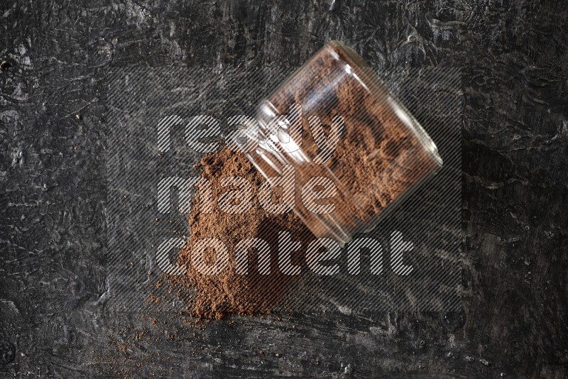A flipped glass jar full of cloves powder on a textured black flooring
