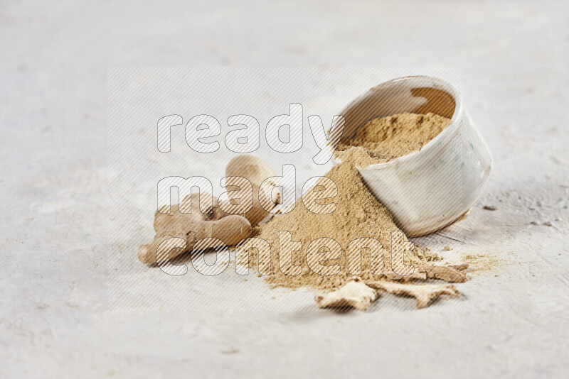 A beige pottery bowl full of ground ginger powder with fallen powder from it on white background