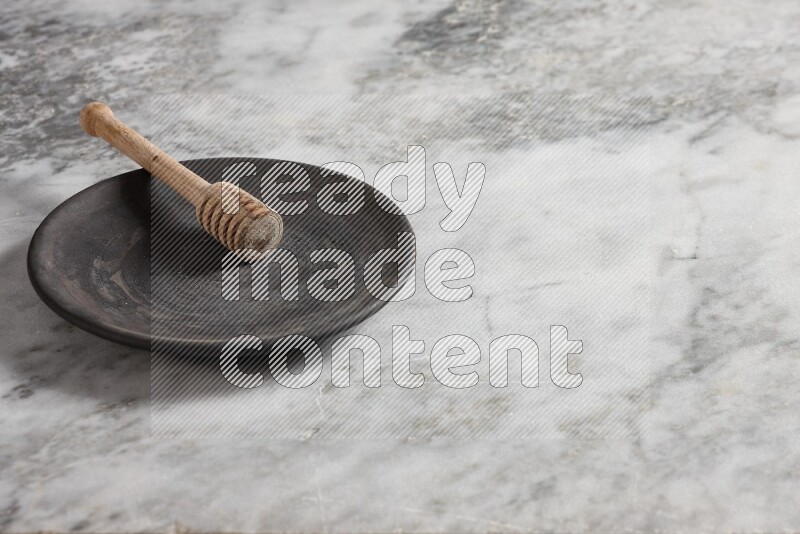 Black pottery plate with wooden honey dipper in it on grey marble background