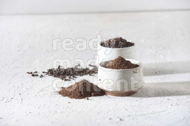 2 Beige ceramic bowls, one full of cloves and the other full of powder on textured white flooring