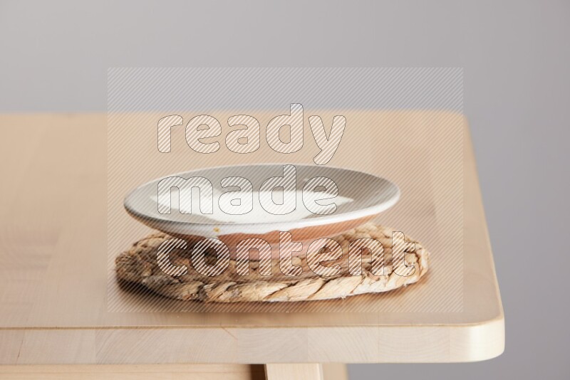 multi-colored pottery Plate placed on a small light colored straw placemat on the edge of wooden table
