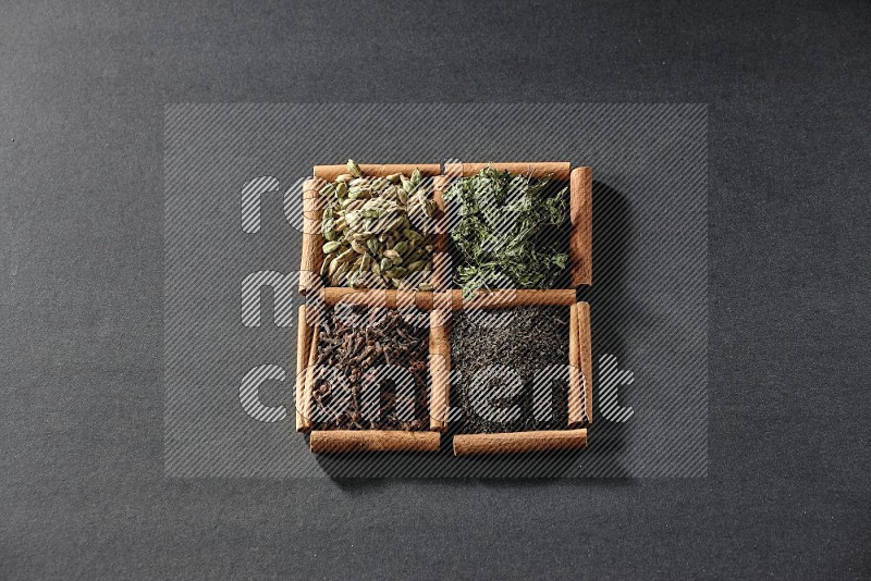 4 squares of cinnamon sticks full of black tea, cloves, dried mint leaves and cardamom on black flooring