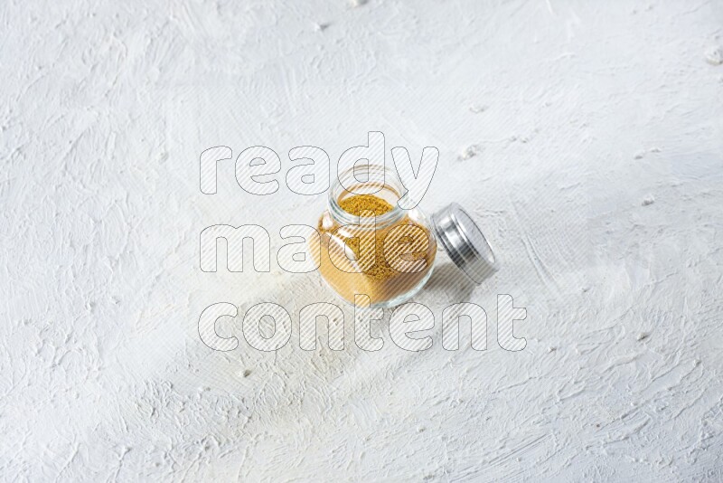 A glass spice jar full of turmeric powder on a textured white flooring