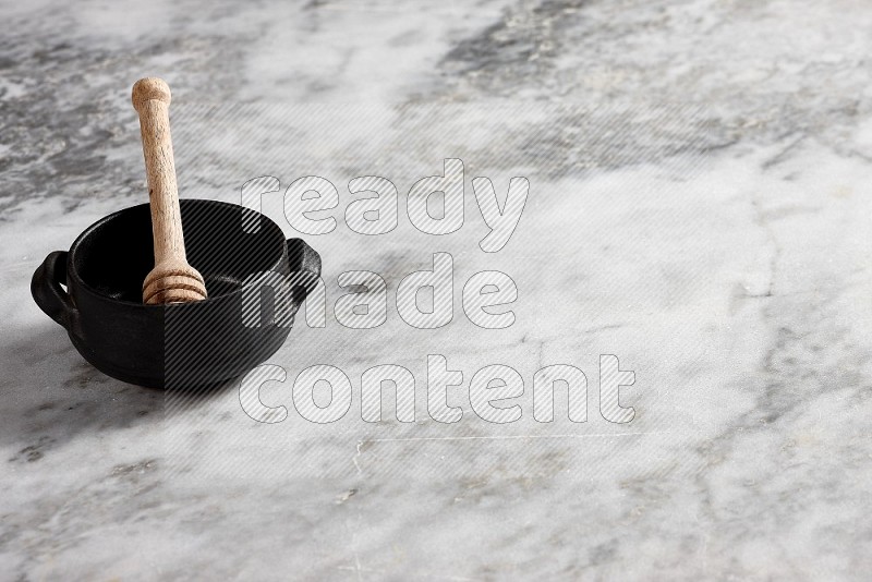 Black Pottery bowl with wooden honey handle in it, on grey marble flooring, 45 degree angle