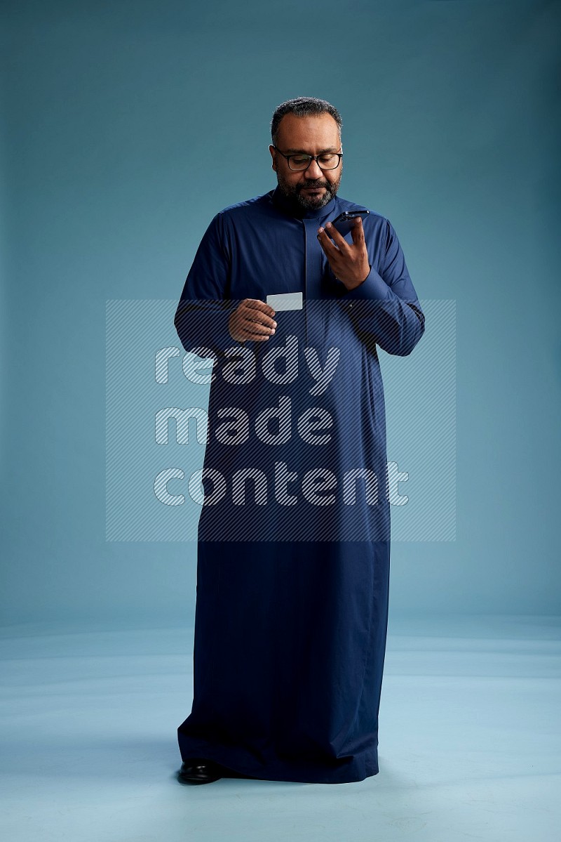 Saudi Man without shimag Standing holding ATM while talking on phone on blue background