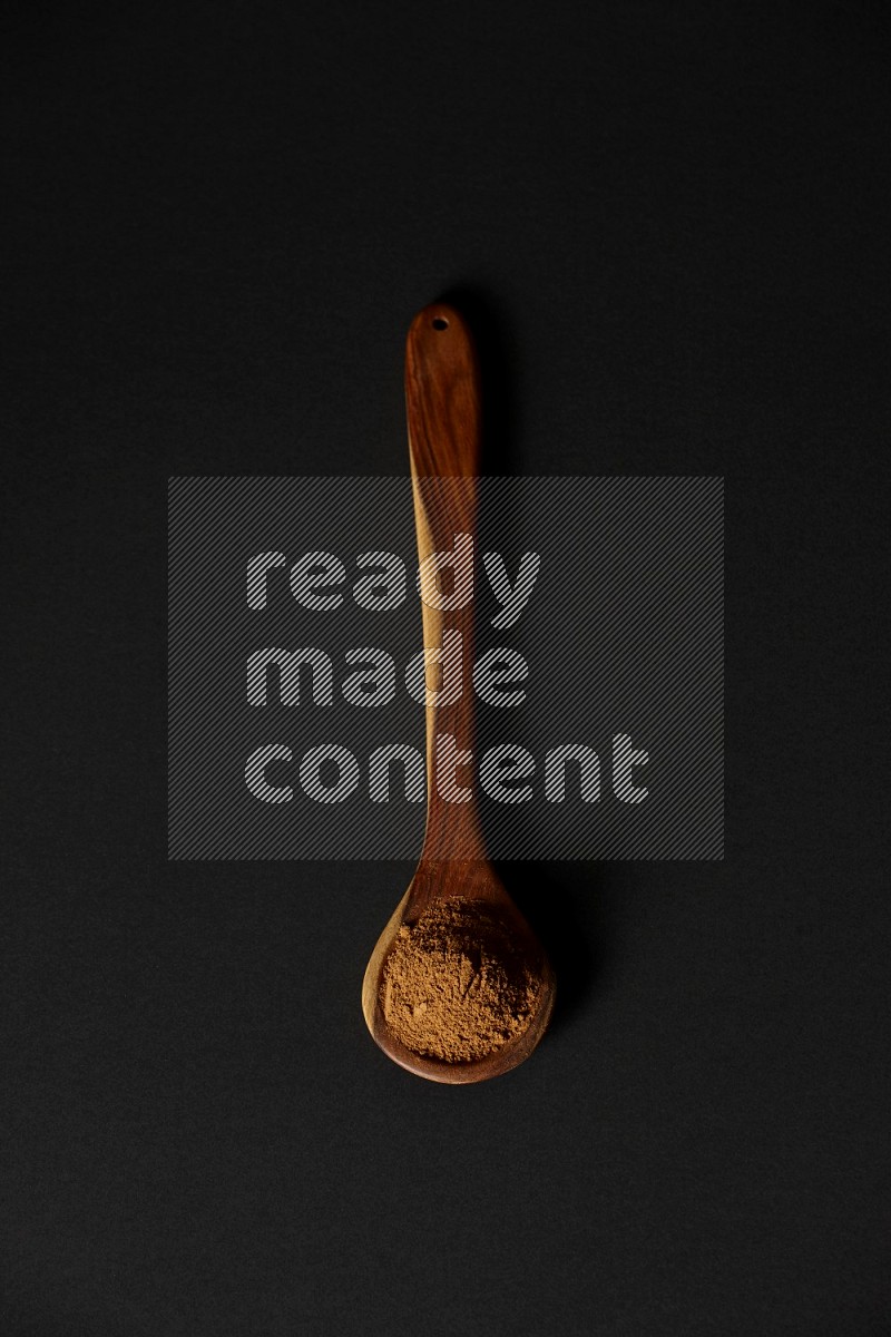 Cinnamon powder in a spoon ladle on black background