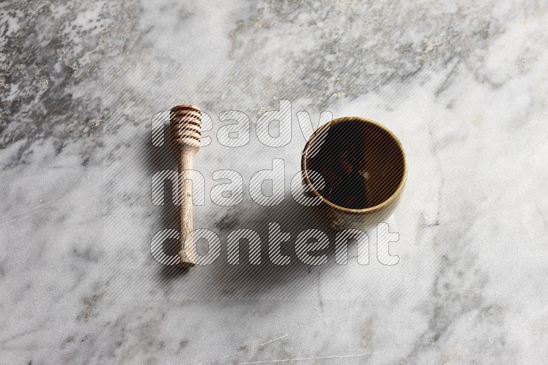 Multicolored Pottery Cup with wooden honey handle on the side with grey marble flooring, 65 degree angle