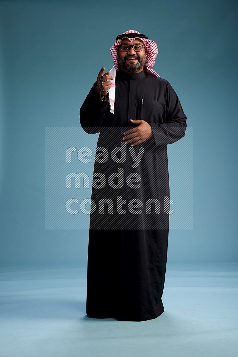 Saudi Man with shimag Standing Interacting with the camera on blue background