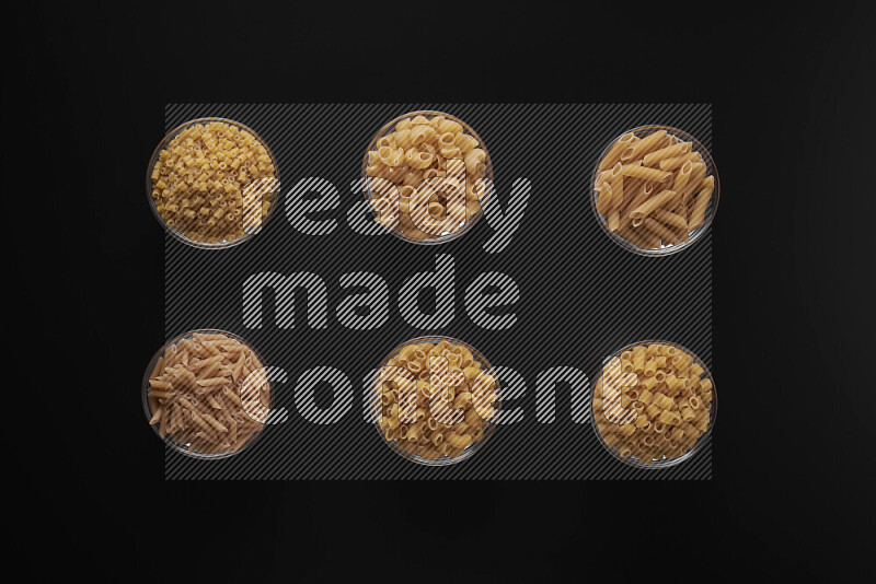 Different pasta types in 6 glass bowls on black background