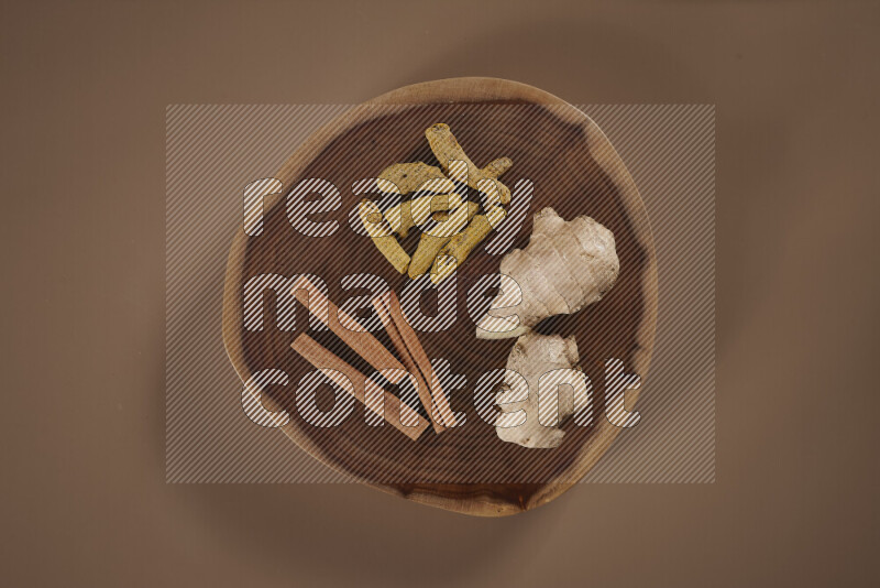 An assorted whole spices on a flat wooden tray including fresh and dried ginger, cinnamon sticks, cardamom, turmeric fingers, cloves, star anise on beige background