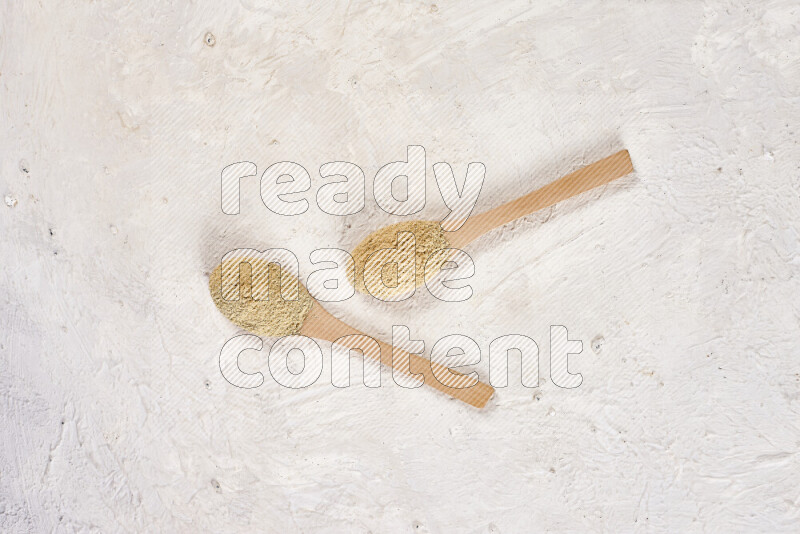 Two wooden spoons full of ground ginger powder on white background