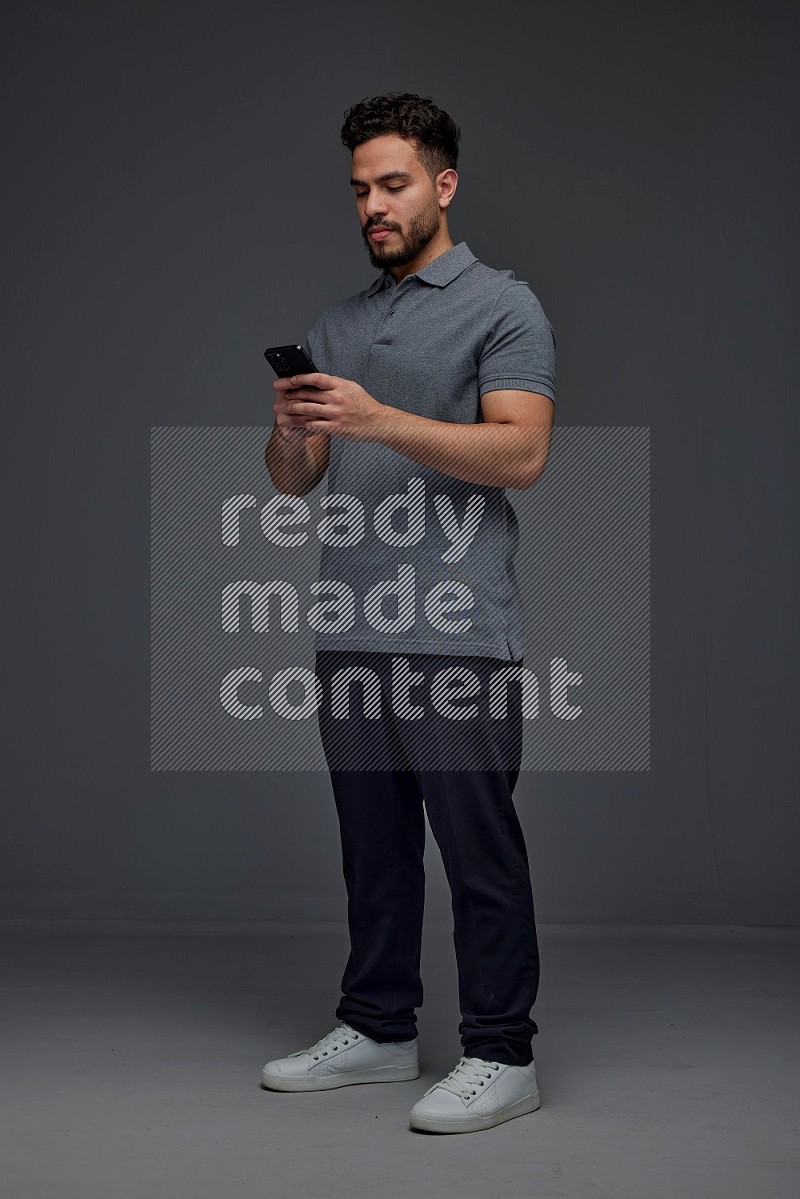 A man wearing casual standing and using his phone eye level on a gray background