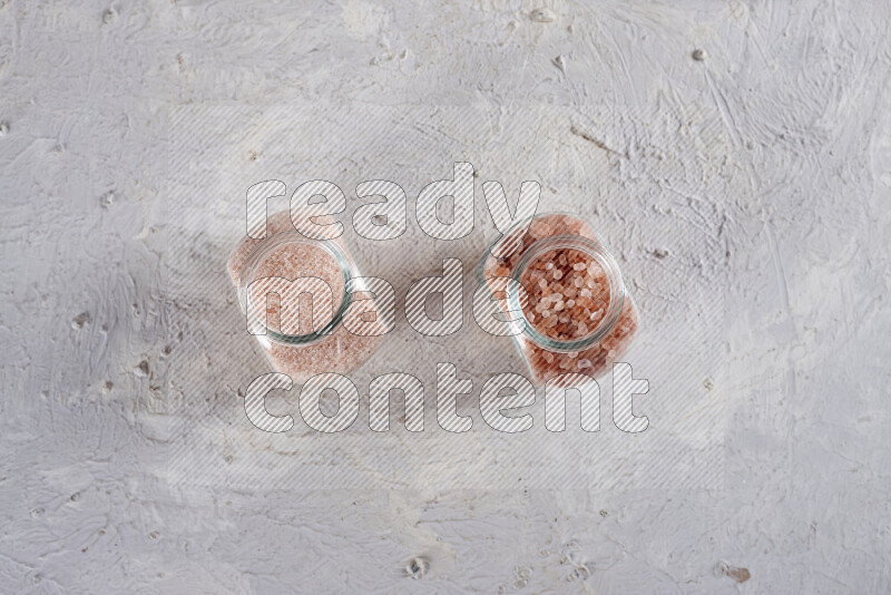 2 glass jars one is filled with fine himalayan salt and the other with coarse himalayan salt on white background