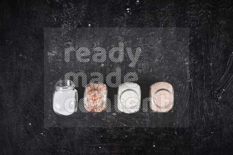 4 glass jars filled with table salt, coarse sea salt, fine himalayan salt and coarse himalayan salt on black background