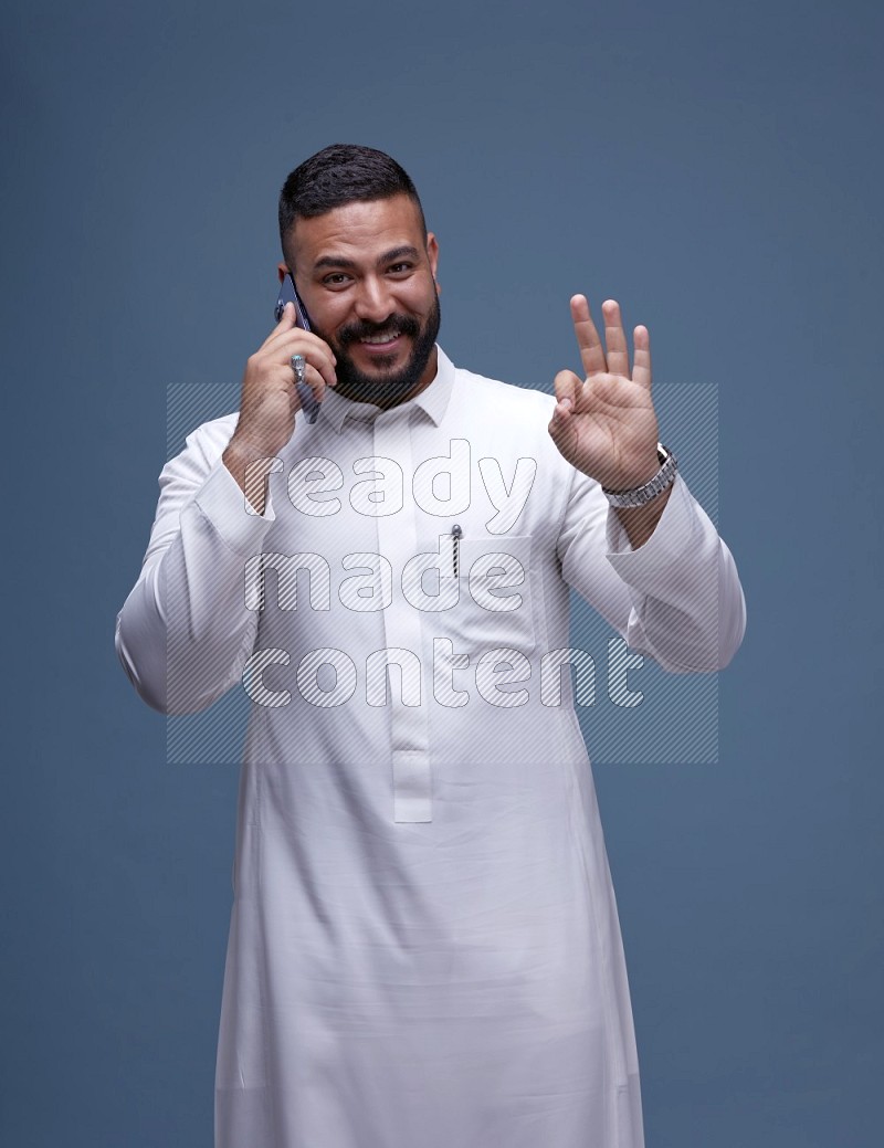 A Saudi man calling on blue background wearing Saudi Thob