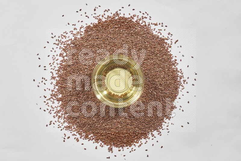 A glass jar full of flaxseeds oil surrounded by flax seeds on a white flooring