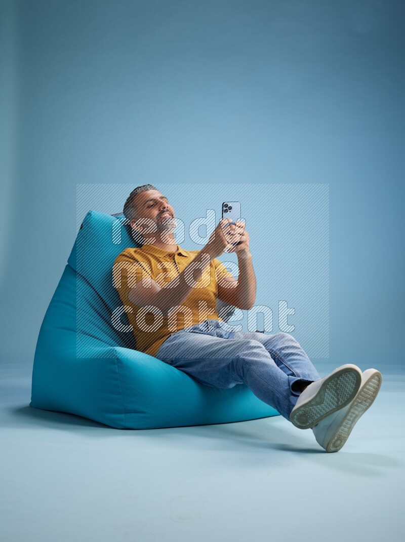 A man sitting on a blue beanbag and texting on phone
