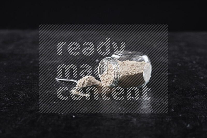 A glass jar full of onion powder flipped with some spilling powder on black background