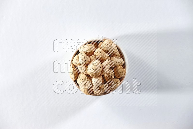 A beige ceramic bowl full of almonds on a white background in different angles