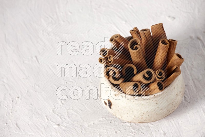 Cinnamon sticks in a beige bowl on a white background