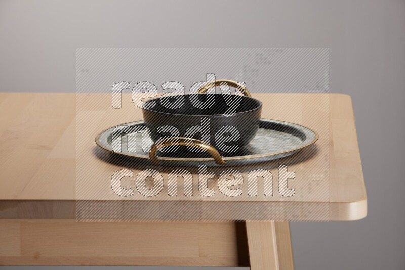 black bowl placed on a rounded stainless steel tray with golden handels on the edge of wooden table