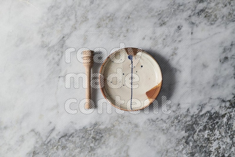 Multicolored Pottery Plate with wooden honey handle on the side on grey marble flooring, Top view