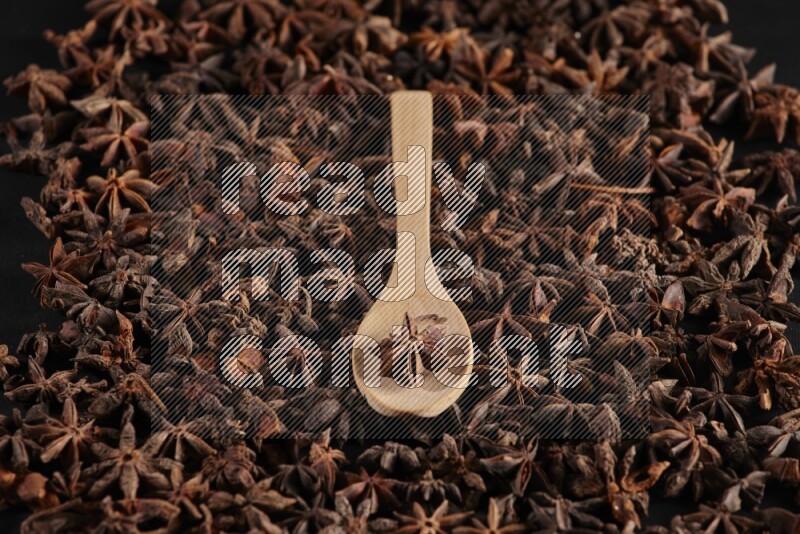 Star Anise in a wooden spoon on more stars anise filling the frame on black flooring