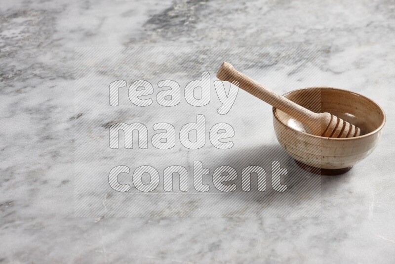 Beige pottery bowl with wooden honey dipper in it on grey marble background