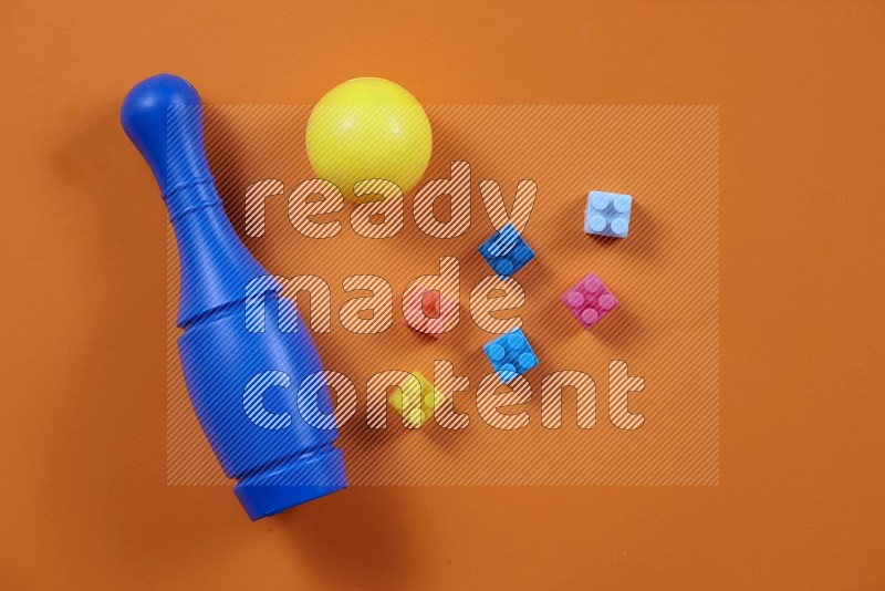 Plastic building blocks, balls and bowling pins on orange background in top view (kids toys)