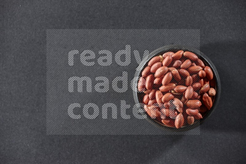 A black pottery bowl full of red skin peanuts on a black background in different angles