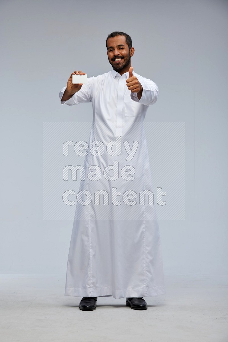 Saudi man wearing Thob standing holding ATM card on Gray background