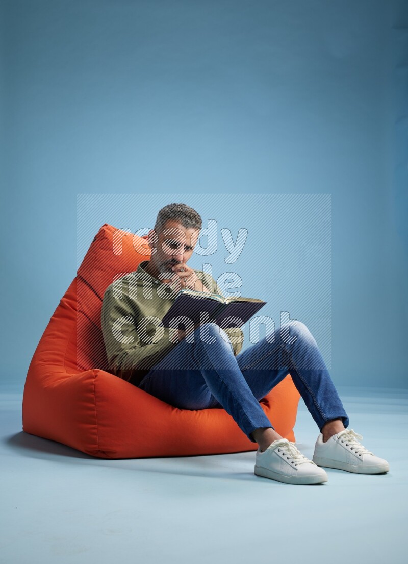 A man sitting on an orange beanbag and reading a book