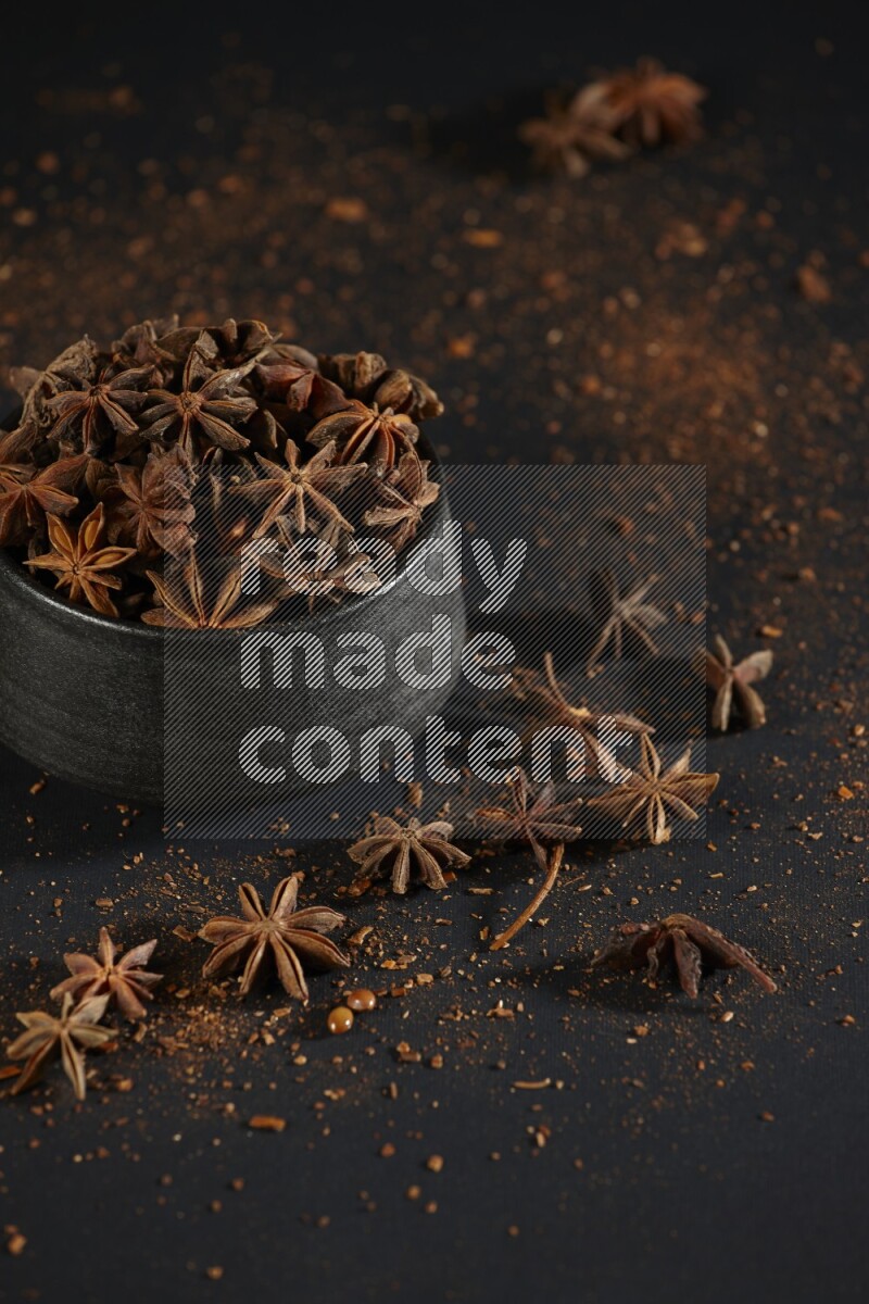 Star Anise in a black bowl with sprinkled anise on black flooring