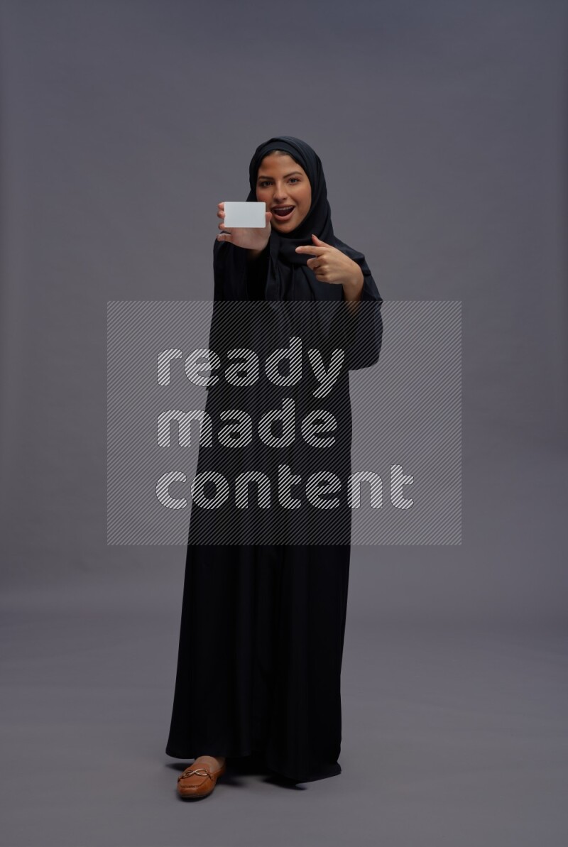 Saudi woman wearing Abaya standing holding ATM card on gray background