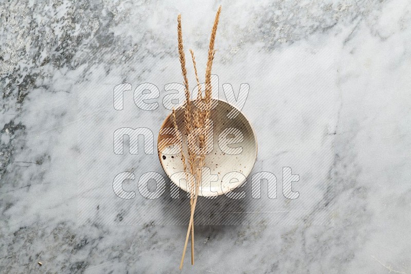 Wheat stalks on Multicolored Pottery Plate on grey marble flooring, Top view