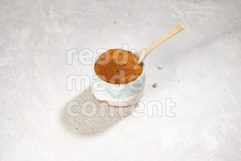 A colored pottery bowl full of ground paprika powder on white background