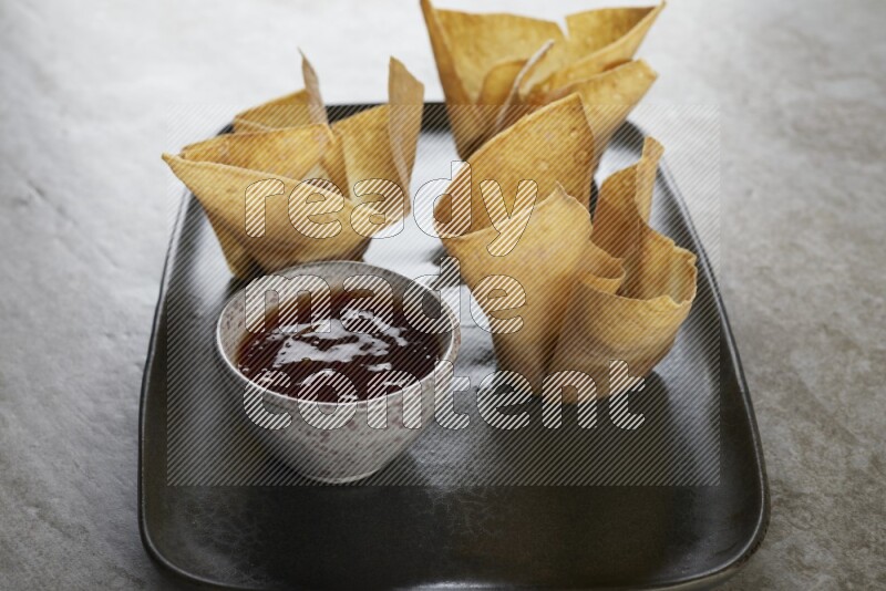 wonton cups with soy sauce ramkin on rectangle dark grey ceramic plate on grey textured counter top