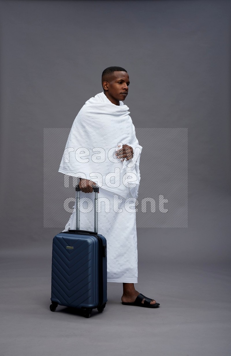 A man wearing Ehram Standing holding traveling bag on gray background