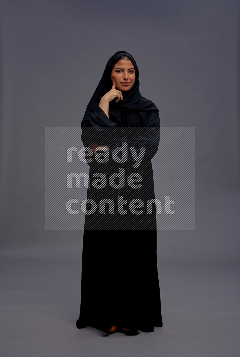 Saudi woman wearing Abaya standing interacting with the camera on gray background