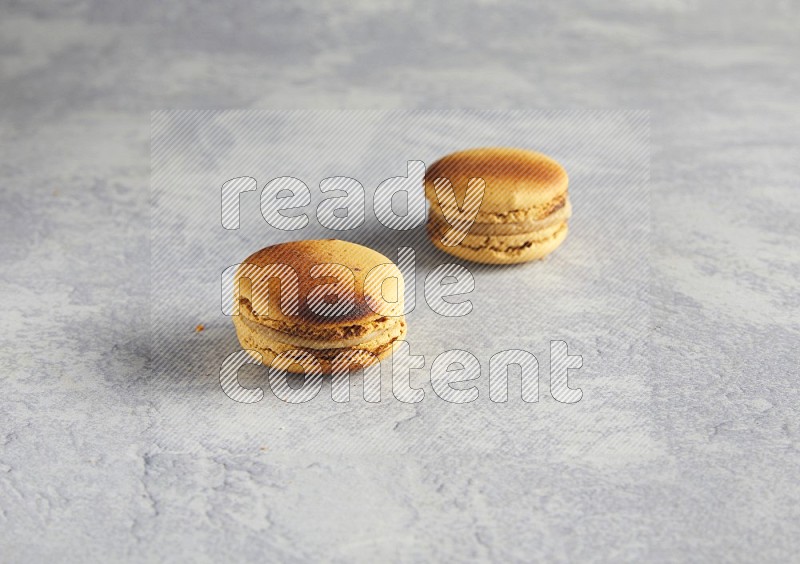 45º Shot of two Yellow Crème Brulée macarons on white  marble background